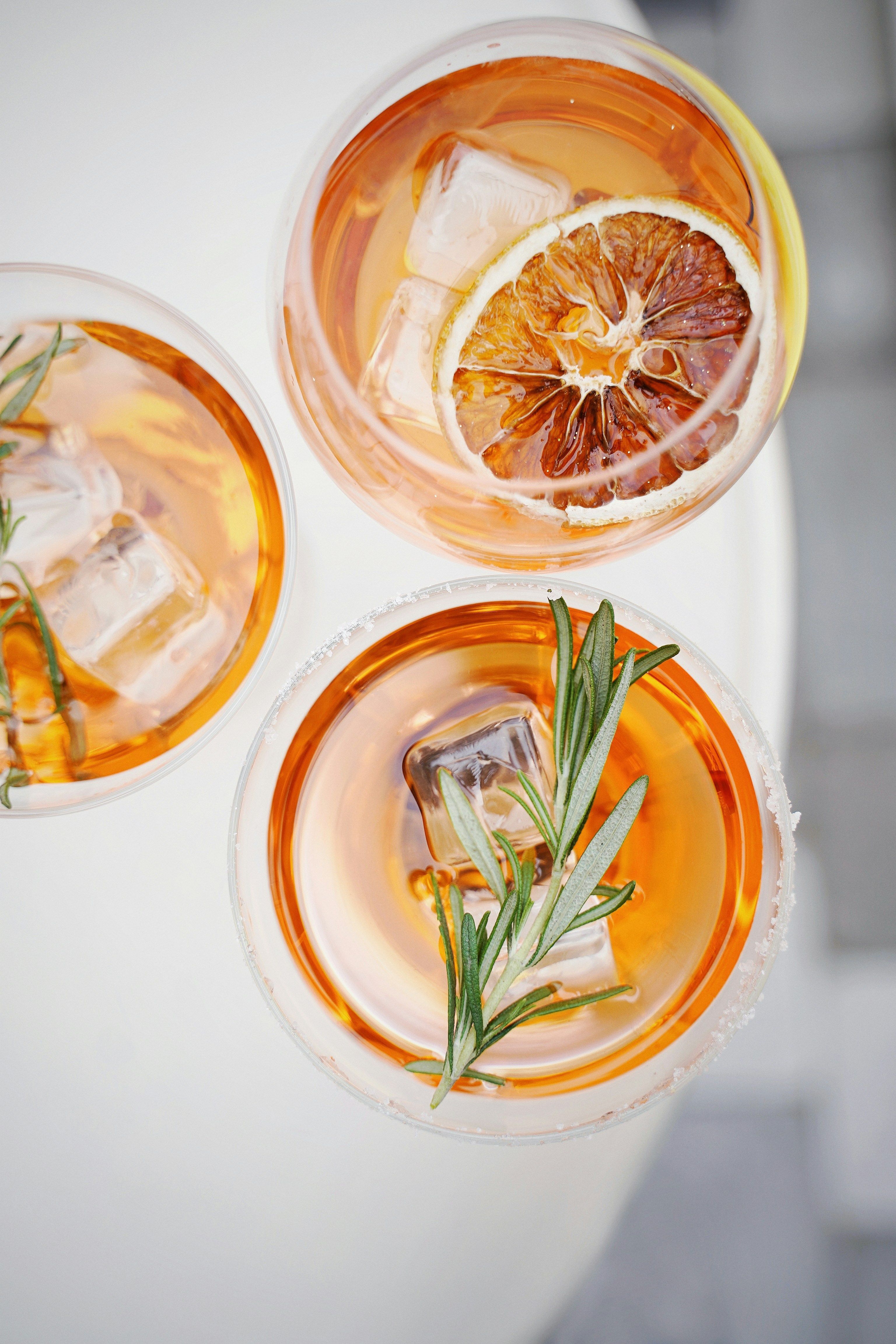 Two cocktails garnished with a dried orange slice and rosemary