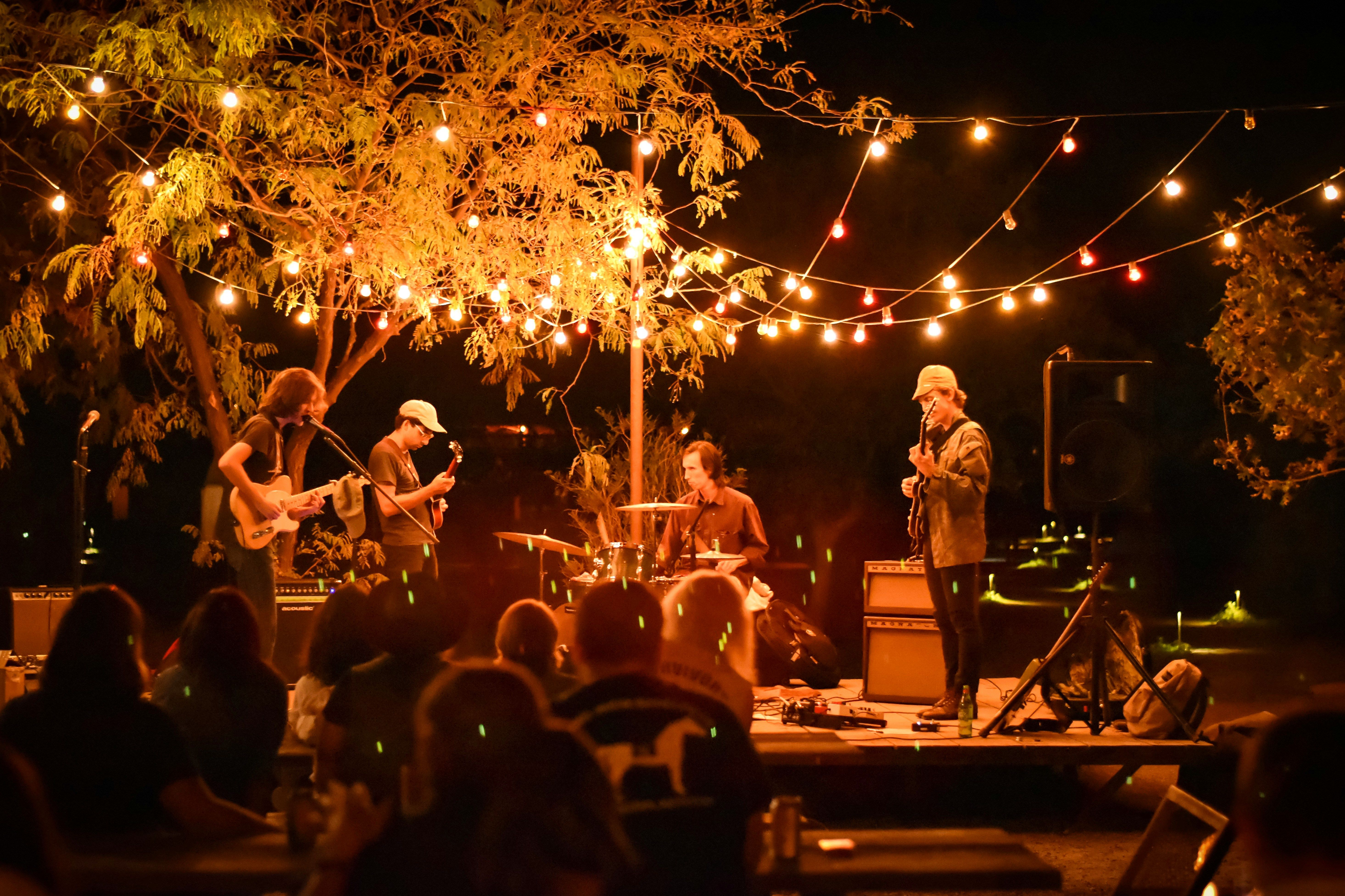 A band performing on an outdoor stage strung with lights