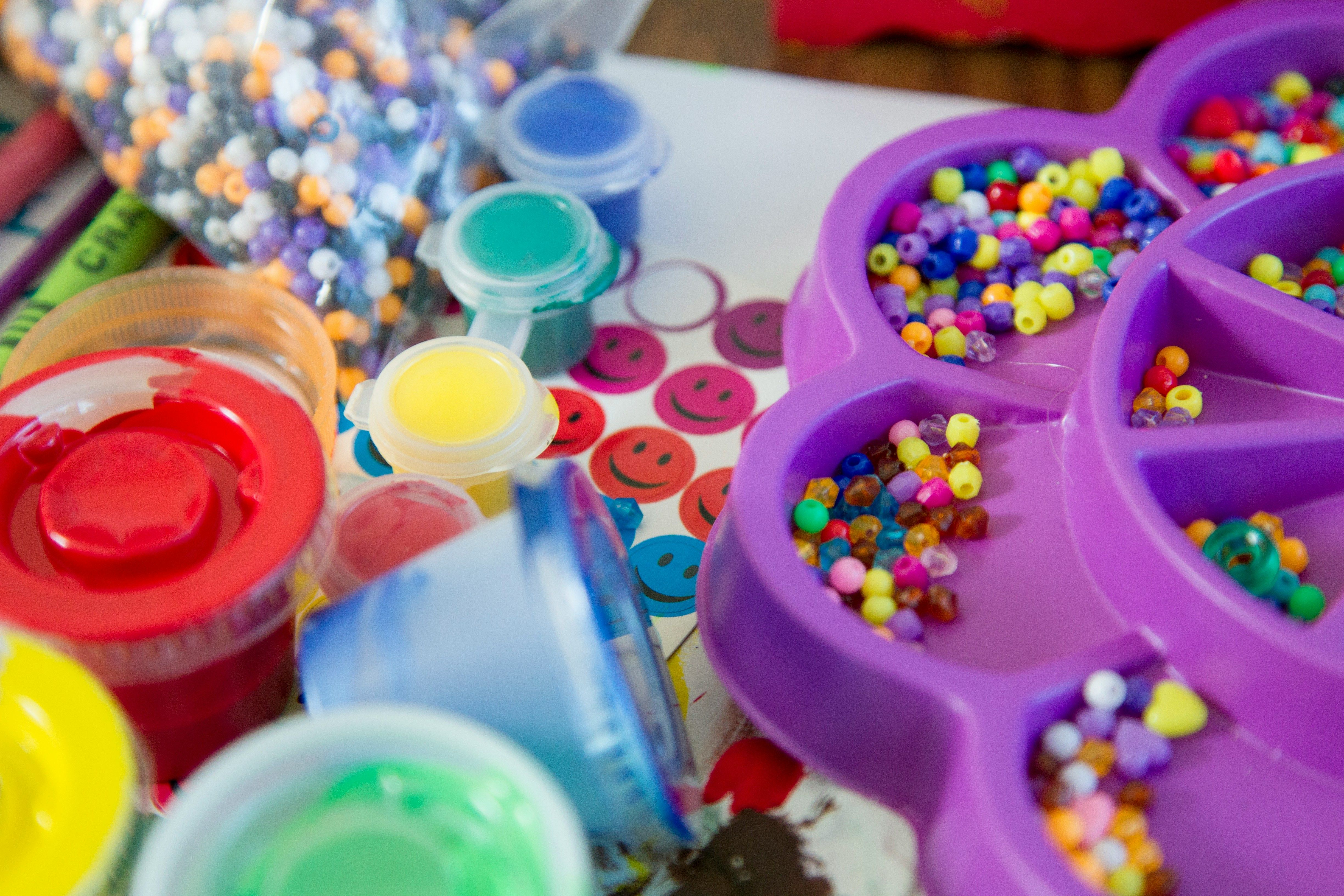 A tray of colourful craft beads next to paint pots and stickers
