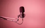 A podcast microphone on a boom arm against a pink background
