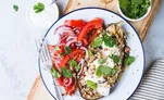 A roasted eggplant plate topped with yogurt, herbs, and a tomato salad